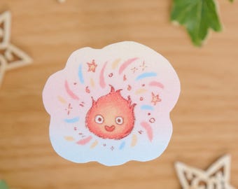 May include: A die-cut sticker featuring a small, round, orange-red flame character with a smiling face, surrounded by pastel pink, yellow, and blue sparkles and stars against a soft, cloud-shaped background with a light blue and pink gradient.