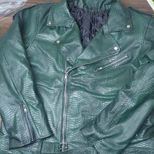 May include: A dark green faux leather motorcycle jacket with a snakeskin texture. The jacket features a notched collar, a diagonal zipper closure, and multiple zippered pockets. It has a belt at the waist and a quilted black lining.