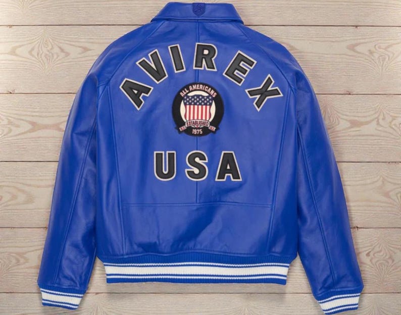 May include: A royal blue leather jacket with the word "AVIREX" arched across the shoulders in white lettering with black outlines. Below the word "AVIREX" is a circular patch with the words "ALL AMERICANS ESTABLISHED 1975" and a US flag design. The word "USA" is below the patch.
