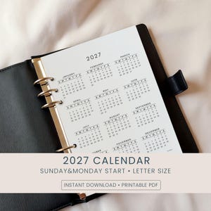 Puede incluir: Una carpeta negra con una inserción de calendario de 2027. El calendario está impreso en papel blanco con un diseño minimalista. El texto "2027 CALENDAR" y "SUNDAY&MONDAY START • LETTER SIZE" son visibles.