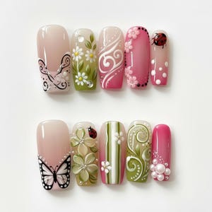 May include: A set of ten artificial nails with various designs. The nails feature a range of colors, including pink, white, and green, with floral, butterfly, and ladybug accents. Some nails have pearl embellishments.