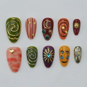 Könnte beinhalten: Eine Sammlung von zehn künstlichen Fingernägeln mit verschiedenen Designs. Die Nägel zeigen Farben wie Grün, Rot, Orange und Gelb, mit goldenen, silbernen und blauen Verzierungen. Designs umfassen Wirbel, Sterne, Monde, Sonnen und ein Herz.