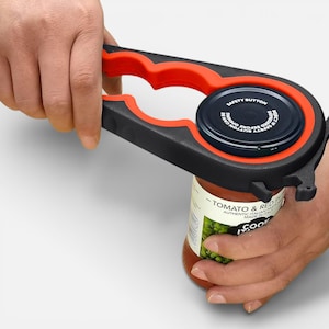May include: A black and red jar opener is used to open a jar of tomato and red sauce. The jar opener has a multi-functional design with a safety button on the lid. The jar is labeled "TOMATO & RED" and "AUTHENTIC ITALIAN MADE".