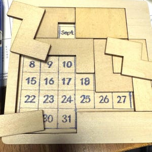 May include: A wooden puzzle calendar with the month of September and numbered days from 8 to 31. The puzzle pieces are light brown, and the numbers are written in blue ink. The word "Sept" is visible.