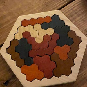 May include: Wooden hexagon puzzle with colorful, interlocking pieces in shades of brown, orange, and black. The puzzle is set on a wooden surface, showcasing the natural wood grain.