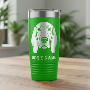 May include: A green travel tumbler with a white graphic of a dog's face. The text "DOG'S NAME" is printed below the dog's face. The tumbler has a silver lid and a ridged base.