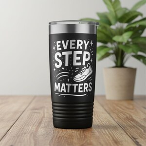 May include: Black insulated tumbler with a silver rim. The tumbler features the text "EVERY STEP MATTERS" in white, along with a white illustration of a running shoe. The tumbler is designed for hot or cold beverages.