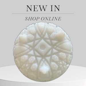 Puede incluir: Un plato decorativo blanco y redondo con un patrón geométrico en relieve detallado. El plato tiene un diseño central y está sostenido por pequeños pies. El texto "NEW IN" y "SHOP ONLINE" se muestra encima del plato.