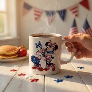 Puede incluir: Una taza de cer&aacute;mica blanca con un gr&aacute;fico de Daisy Duck y Minnie Mouse vistiendo conjuntos y zapatillas con estampado de estrellas en rojo, blanco y azul. La taza contiene una bebida caliente oscura con vapor visible, sostenida por una mano.