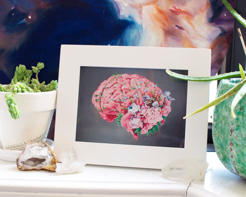 May include: A framed print of a pink human brain with flowers and leaves growing from it. The brain is on a dark gray background.