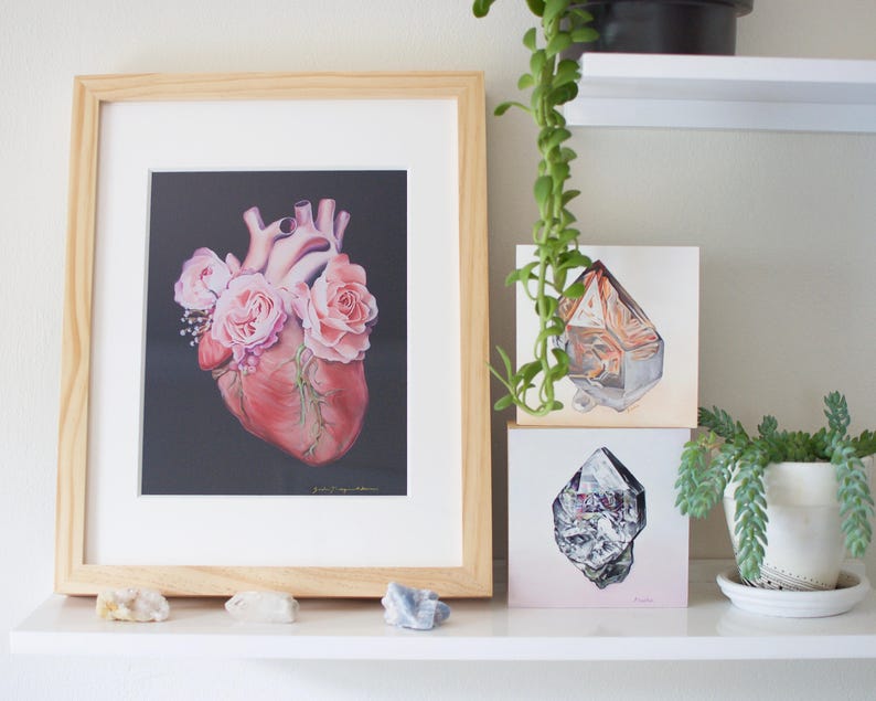 May include: A framed print of a realistic anatomical heart with pink roses growing from it, displayed on a shelf with two framed prints of crystals.