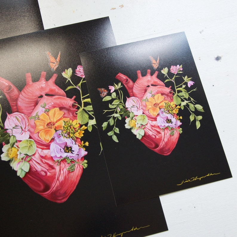 May include: A black background with a red anatomical heart surrounded by pink, yellow, and white flowers. The flowers are arranged around the heart in a circular pattern. The image is a digital illustration.