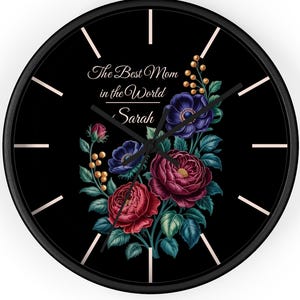 Puede incluir: Reloj de pared negro con un diseño floral con flores rojas, moradas y azules. La esfera del reloj incluye el texto "The Best Mom in the World Sarah". El reloj tiene manecillas e indicadores de hora blancos.