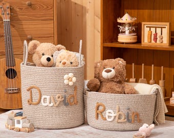 May include: Two beige woven rope storage baskets featuring embroidered names. The taller basket displays the name David with a small flower accent, while the shorter basket features the name Robin. Both baskets contain plush teddy bears.