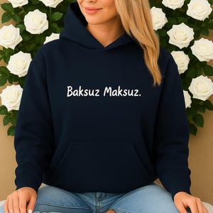 Könnte beinhalten: Marineblauer Kapuzenpullover mit dem weißen Text "Baksuz Maksuz." Der Hoodie hat eine Vordertasche und eine Kapuze. Die Person trägt hellblaue Jeans mit einem zerrissenen Knie.
