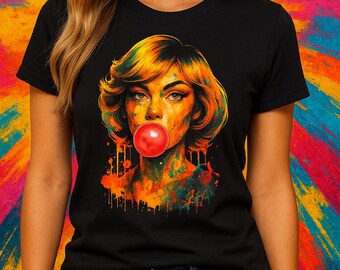 Può includere: Una t-shirt nera con una stampa grafica colorata di una persona con i capelli corti che soffia una bolla di gomma da masticare rosso brillante. L'opera utilizza uno stile a pittura schizzata con toni arancioni, gialli e blu sul viso.