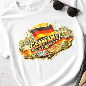 Op de afbeelding: Wit T-shirt met een kleurrijke illustratie van Duitse culturele elementen. Het ontwerp bevat de Duitse vlag, het woord "Duitsland", bier, worstjes en een traditionele hoed. Zonnebril ligt op het shirt.