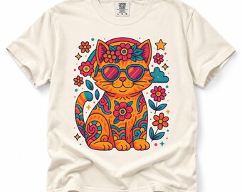 May include: A cream-colored short-sleeve t-shirt featuring a graphic of an orange cat wearing heart-shaped sunglasses and a flower crown. The cat is decorated with colorful floral and swirl patterns, surrounded by small flowers, stars, and clouds.