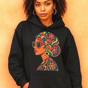 Könnte beinhalten: Schwarzer Kapuzenpullover mit einem farbenfrohen Retro-Grafikdesign einer Frau mit Sonnenbrille und Blumenhaar. Das Design enthält orange, rote, gelbe und türkisfarbene Elemente. Der Hoodie hat eine Vordertasche und eine Kapuze.