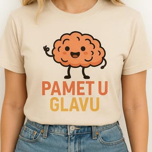 Könnte beinhalten: Beiges T-Shirt mit einem Cartoon-Gehirn mit lächelndem Gesicht und dem Text "PAMET U GLAVU" in Orange und Gelb. Das T-Shirt wird mit Jeansshorts getragen. Das Bild zeigt eine Person.