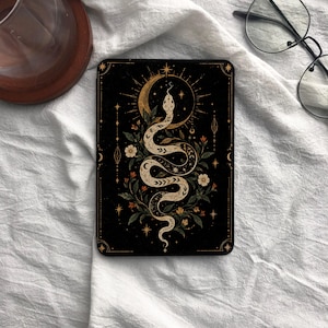May include: A rectangular black tablet case featuring a central illustration of a coiled snake surrounded by botanical elements, a crescent moon, and radiating stars. The design uses gold and white lines against a solid black background.