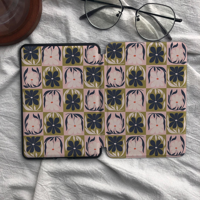 Puede incluir: Una funda para lector electr&oacute;nico con un patr&oacute;n de tablero de ajedrez repetitivo de flores azul marino oscuro sobre un fondo rosa claro y flores rosa claro sobre un fondo verde oliva. La funda est&aacute; abierta, mostrando el dise&ntilde;o interior y unas gafas.