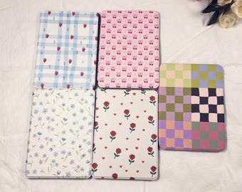 May include: A selection of rectangular cases featuring diverse patterns. Designs include strawberries on blue gingham, cherries on pink, floral prints, roses and hearts on white, and a checkered pattern.