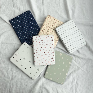 May include: A selection of rectangular notebooks featuring diverse patterns. Designs include white polka dots on navy, red stars on cream, white hearts on white, white bows and hearts on white, red cherries and lips on white, and white daisies on sage green.