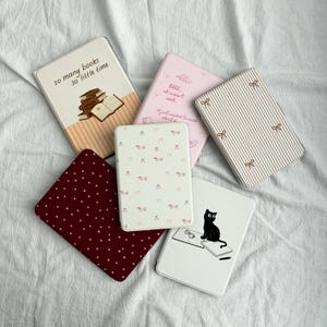 May include: A collection of small notebooks with various designs. One notebook has the text "so many books so little time" with a stack of books. Other notebooks feature patterns like stripes, polka dots, and a cat illustration.