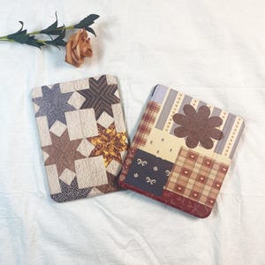 May include: Two decorative cases with patchwork designs. One case features star patterns in various colours, including brown, blue, and gold. The other case has a floral design and a mix of patterns, including plaid and hearts.