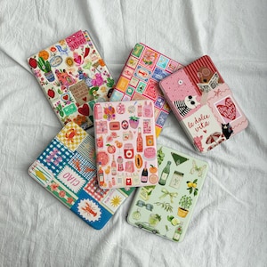 May include: A collection of colorful, patterned tablet cases. Designs include floral, food, and travel themes. One case features the text "la dolce vita". Other cases have images of cacti, fruit, and a lobster.