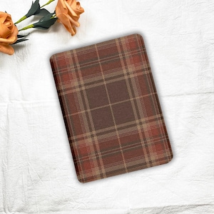 May include: A rectangular, plaid-patterned item in shades of brown, tan, and red. The pattern consists of intersecting lines forming a grid. The item is placed on a white surface, with orange roses in the upper left corner.