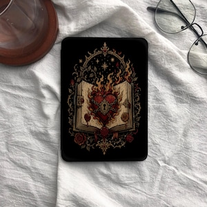 May include: A black e-reader case featuring a central illustration of an open book with a flaming red heart locked by a golden keyhole. The design includes intricate gold filigree, dark red roses, and wax seals, all set against a deep black background.