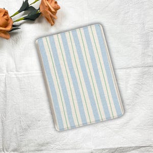 Può includere: Tappeto rettangolare a righe blu e bianche con sottili strisce verdi. Il tappeto ha angoli arrotondati e una superficie strutturata. Il tappeto è posto su una superficie bianca e strutturata. Alcune rose arancioni sono nell'angolo in alto a sinistra.