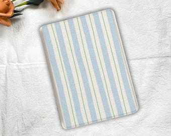 Puede incluir: Alfombra rectangular a rayas azules y blancas con finas rayas verdes. La alfombra tiene esquinas redondeadas y una superficie texturizada. La alfombra está colocada sobre una superficie blanca y texturizada. Unas rosas naranjas están en la esquina superior izquierda.