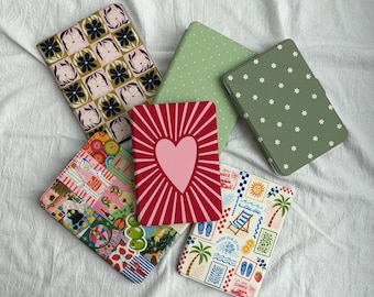 May include: Five rectangular e-reader cases featuring various designs: one with a grid of dark blue flowers and abstract shapes, one solid light green with white dots, one dark green with white flowers, one red with a pink heart, and one with summer-themed stamps.