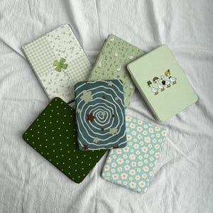 Puede incluir: Una variedad de fundas para tabletas coloridas con varios diseños. Las fundas presentan patrones como un trébol de cuatro hojas, gansos, lunares, estampados florales y un diseño en espiral con estrellas. Las fundas son en tonos verdes, azules y blancos.