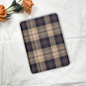May include: A rectangular plaid pattern in navy blue, tan, and brown. The pattern is a classic check design, with intersecting lines creating squares and rectangles. The item is likely a mat or a decorative piece.