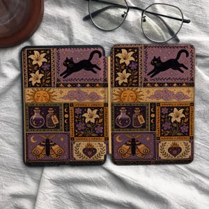 May include: A rectangular e-reader case featuring a repeating pattern of black cats, moths, suns, clouds, potion bottles, and flowers in shades of purple, gold, and black. The design is divided into panels with celestial and botanical motifs.