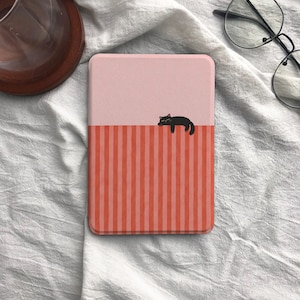 May include: A pink and red striped tablet case with a black cat illustration. The top half of the case is solid pink, while the bottom half features vertical red stripes. A black cat is lying on the edge of the pink section.