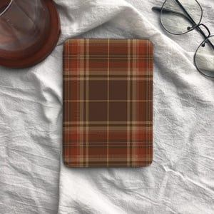 May include: A rectangular e-reader cover featuring a brown, tan, and burnt orange plaid pattern. The design consists of intersecting horizontal and vertical lines forming a classic tartan grid across the entire surface of the device case.