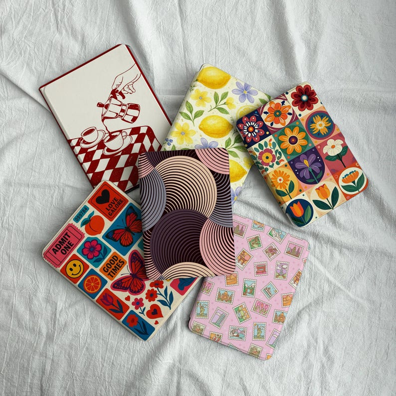 May include: Five rectangular e-reader cases featuring diverse designs: a red and white checkered pattern with a coffee pot, a yellow lemon print, a colorful floral grid, a geometric circle pattern, and a pink grid with small postage stamp illustrations.
