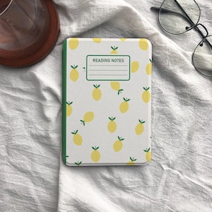 May include: A notebook with a white cover featuring a pattern of yellow lemons with green leaves. The notebook has a green spine and the text "READING NOTES" in a green rectangle.