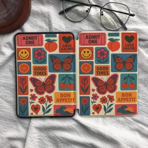 May include: A protective case for an e-reader featuring a repeating pattern of butterflies, flowers, cherries, peaches, smiley faces, and hearts. The design includes text boxes reading ADMIT ONE, LOVE GALORE, GOOD TIMES, and BON APPETIT.