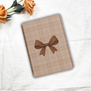 May include: A rectangular, beige notebook with a brown bow illustration in the center. The notebook has a plaid pattern and is surrounded by a white background with orange roses.