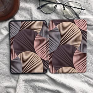 May include: A protective e-reader cover featuring a repeating pattern of overlapping circles in shades of dark purple, light purple, and soft pink. The design consists of thin, concentric lines forming circular shapes across the entire surface of the case.
