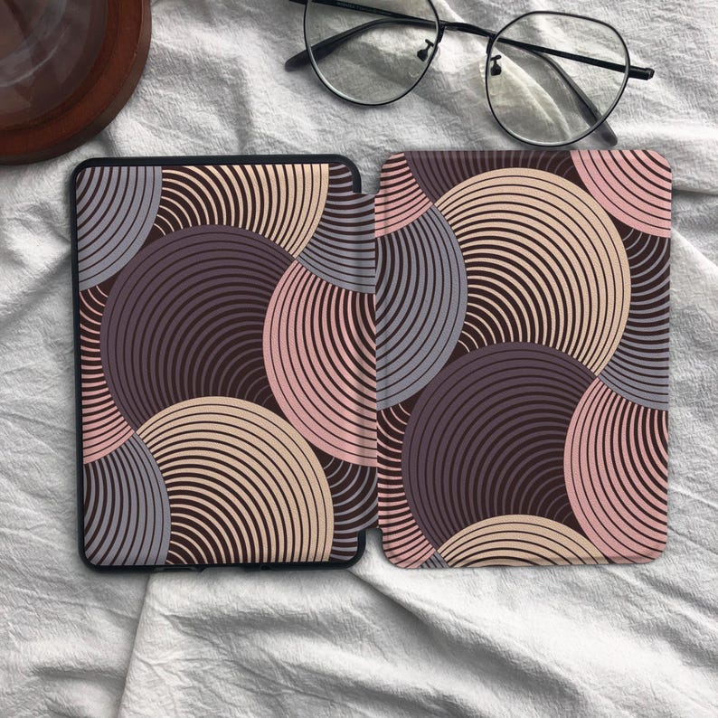 May include: A protective e-reader cover featuring a repeating pattern of overlapping circles in shades of dark purple, light purple, and soft pink. The design consists of thin, concentric lines forming circular shapes across the entire surface of the case.