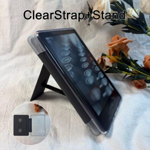 May include: A clear protective case for an e-reader featuring an integrated black kickstand and a hand strap on the back. The case is shown attached to a device, with an inset image displaying the open case structure and the text ClearStrap+Stand.