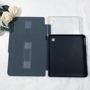 Pode incluir: Uma capa de tablet cinza escuro com uma capa de pl&aacute;stico transparente e uma capa de tablet preta. A capa cinza escuro tem um suporte embutido com uma al&ccedil;a el&aacute;stica. A capa transparente est&aacute; aberta e a capa preta est&aacute; aberta.