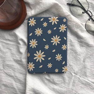 May include: A rectangular e-reader cover featuring a dark blue background with a repeating pattern of white daisies with yellow centers. The cover is positioned flat, displaying a consistent floral motif across its entire surface area.